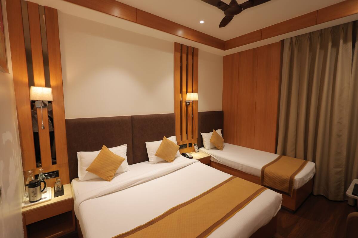 A hotel room with two beds, wooden headboards, bedside tables with lamps, a minibar, and a window with curtains.