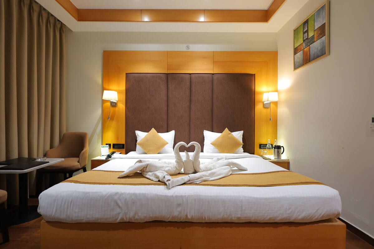 A hotel room with a large bed, two bedside lamps, a desk, a chair, and a painting on the wall.