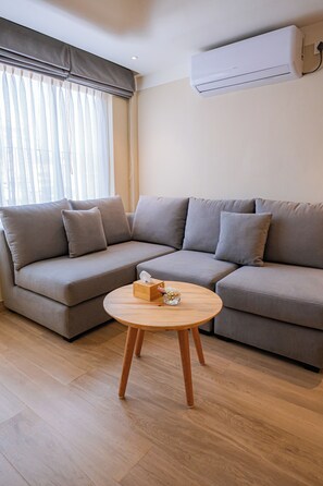 Een woonkamer met een hoekbank, een ronde houten salontafel en een wandgemonteerde airconditioning.