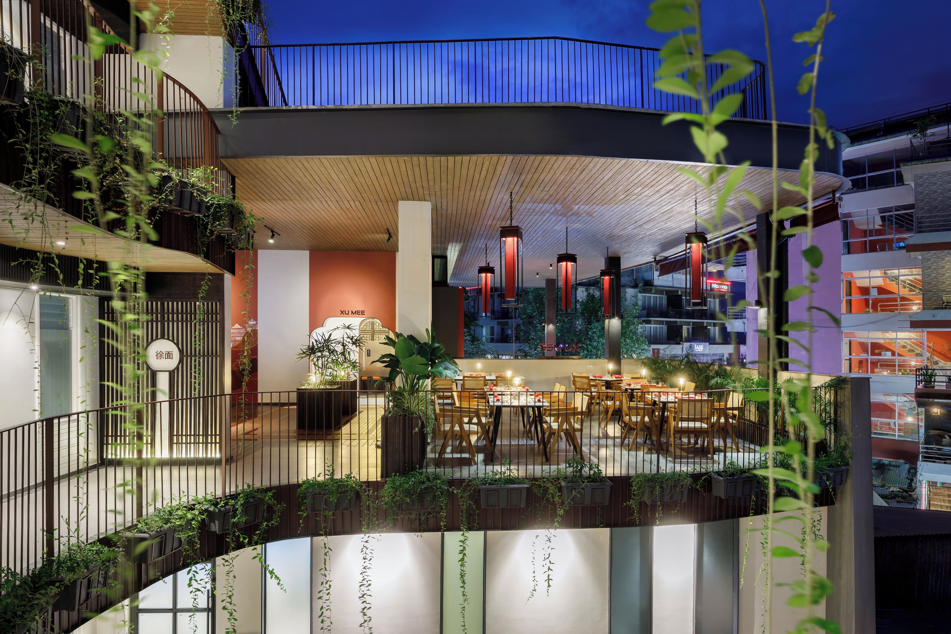 Un espace de restauration intérieur moderne, avec des tables et des chaises, entouré de plantes et doté d’un plafond en bois.