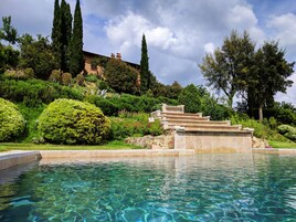 Una piscina con agua cristalina, rodeada de exuberante vegetación y una escalera de piedra que conduce a un edificio.