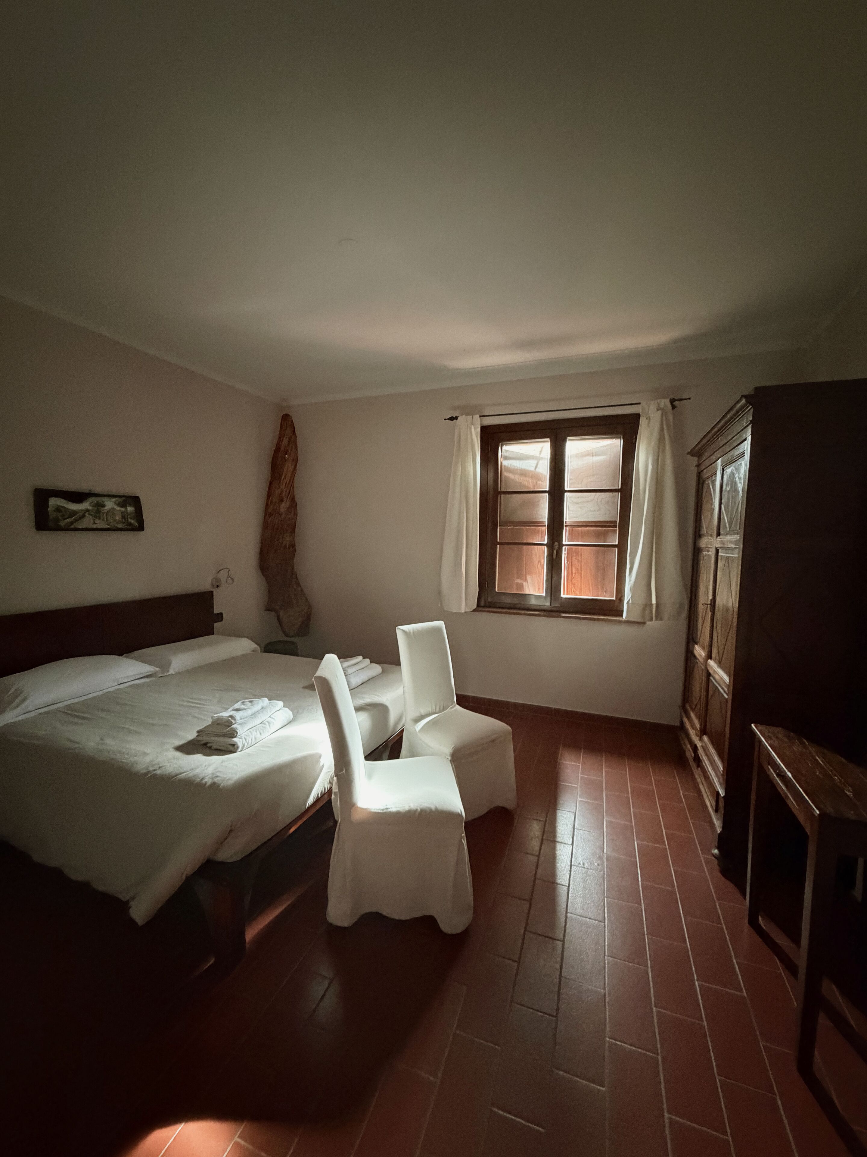 Un dormitorio con una cama, dos sillas, un armario de madera y una ventana con cortinas.