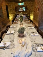 Una larga mesa de comedor lista para una comida en una habitación con paredes de piedra y un televisor en la parte superior.