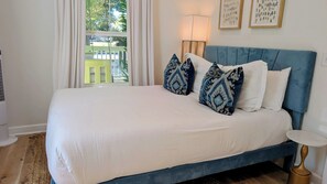Ein Bett mit blauer Kopfteil, weißer Bettwäsche und gemusterten Kissen.