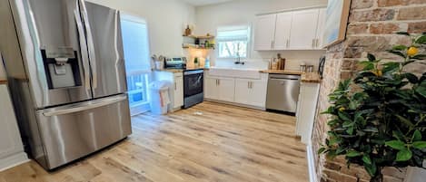 A modern kitchen with stainless steel appliances, white cabinets, and a wooden floor.