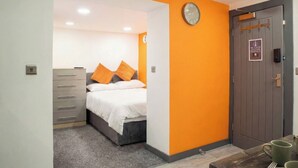 A bedroom with a bed, a dresser, an orange wall, a clock, and a door with a sign. - City Centre Studio | Fast Wi-Fi | Workspace | Washer/Dryer | Netflix | Air Fryer (Bradford)