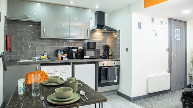 A compact kitchen with grey cabinets, a microwave, a toaster, and a small oven. - City Centre Studio | Fast Wi-Fi | Workspace | Washer/Dryer | Netflix | Air Fryer (Bradford)