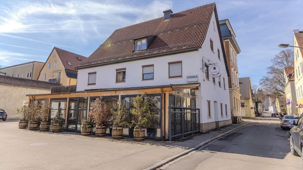 Ein zweistöckiges Gebäude mit Restaurant im Erdgeschoss, ausgestattet mit großen Fenstern und Pflanzen in Kübeln.