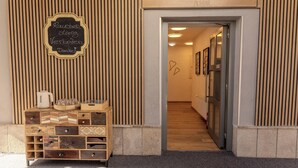 Eine Holzfassade mit einem Schild mit der Aufschrift 'CHAPLIN GÄTTEHAUS PILS-BAR' und einer Tafel mit Text. Ein Holzkabinett mit Schubladen und einem Wasserkocher ist sichtbar.