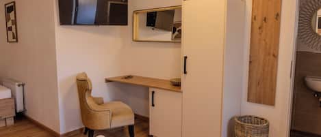 A bedroom with a bed, a wardrobe, a desk, a chair, a mirror, a radiator, and a bathroom with a sink and a mirror.