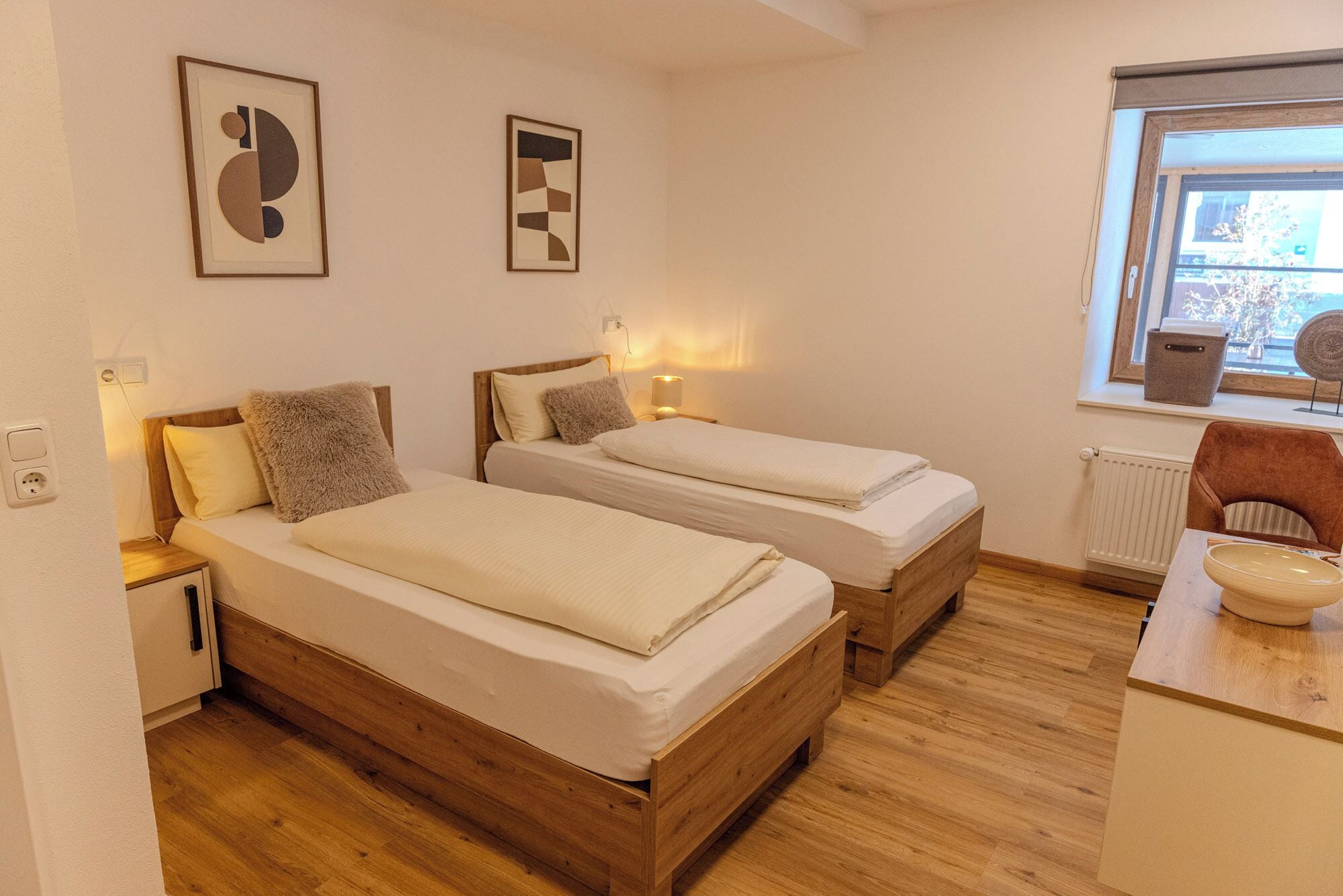Una habitació amb dos llits de fusta, un escriptori, una cadira i dues obres d'art penjades a la paret.