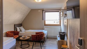 Ein kleines Zimmer mit Bett, zwei Stühlen, einem kleinen Tisch, einem Fenster und einer Heizung.