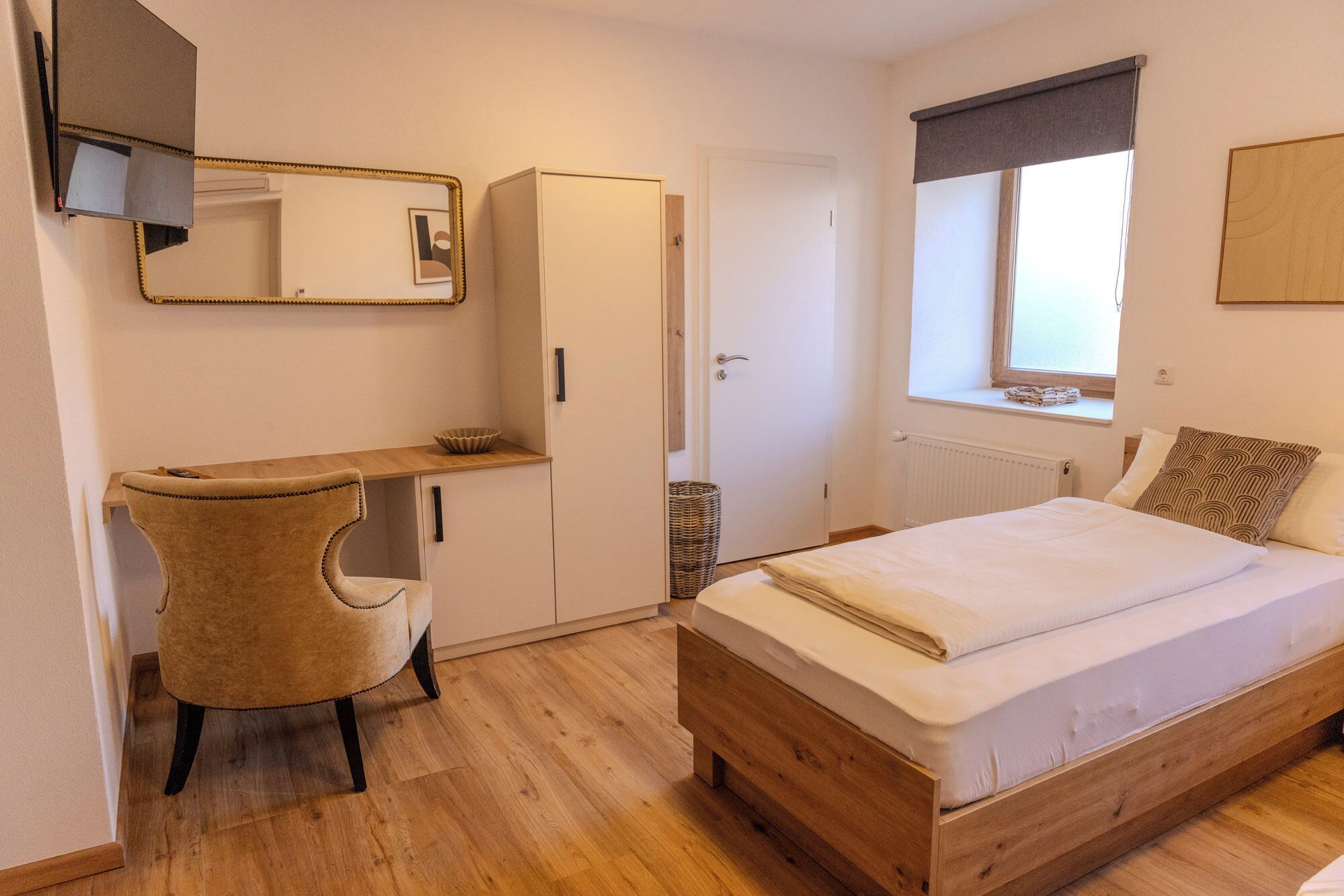 A bedroom with a bed, a chair, a wardrobe, a mirror, and a window with a view.