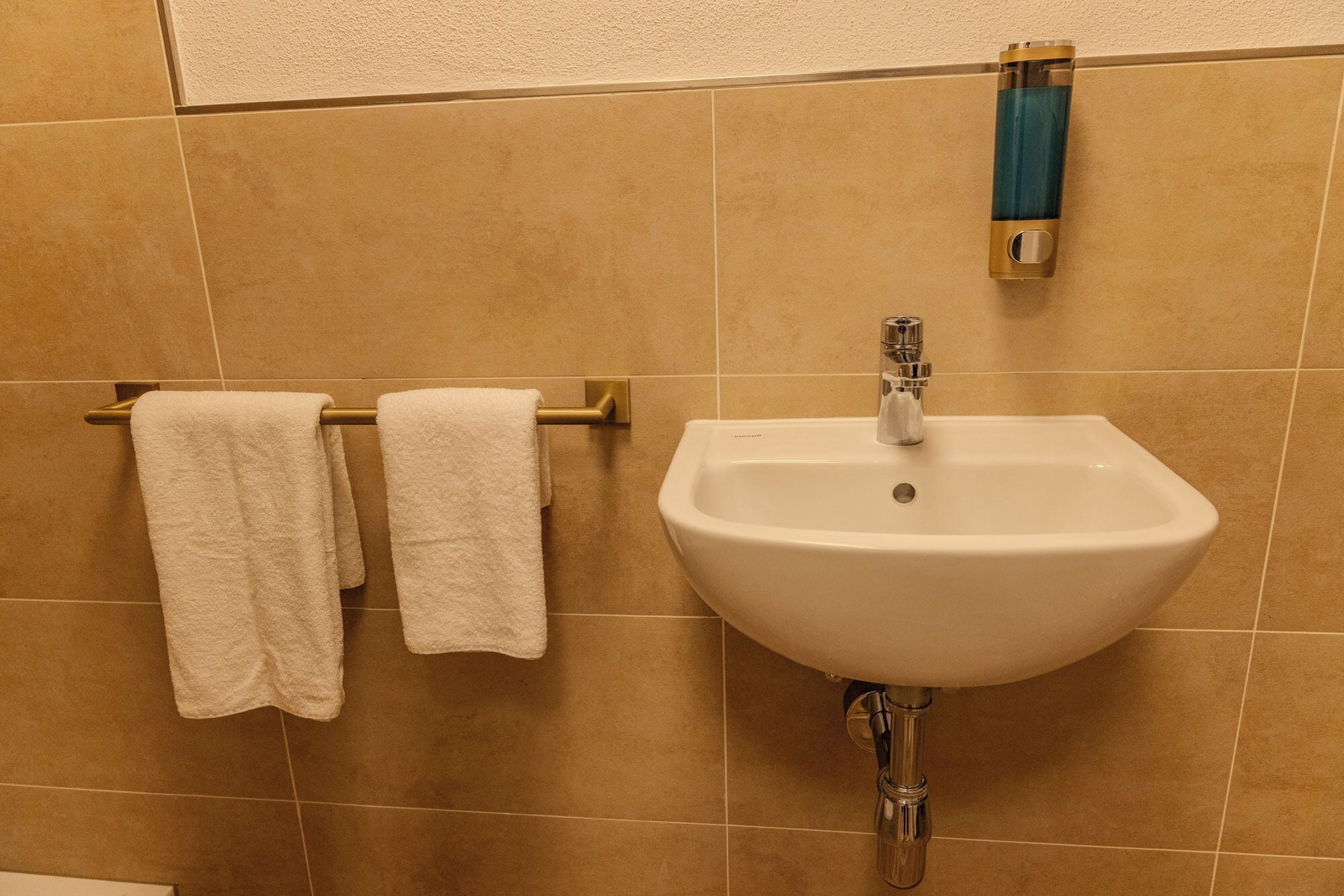 Ein Badezimmer mit einem weißen Waschbecken, einem Handtuchhalter mit zwei weißen Handtüchern und einem blauen Seifenspender.