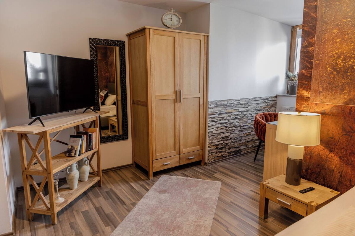 Une chambre avec une télévision, une armoire en bois, un mur en pierre et une table de chevet avec une lampe.