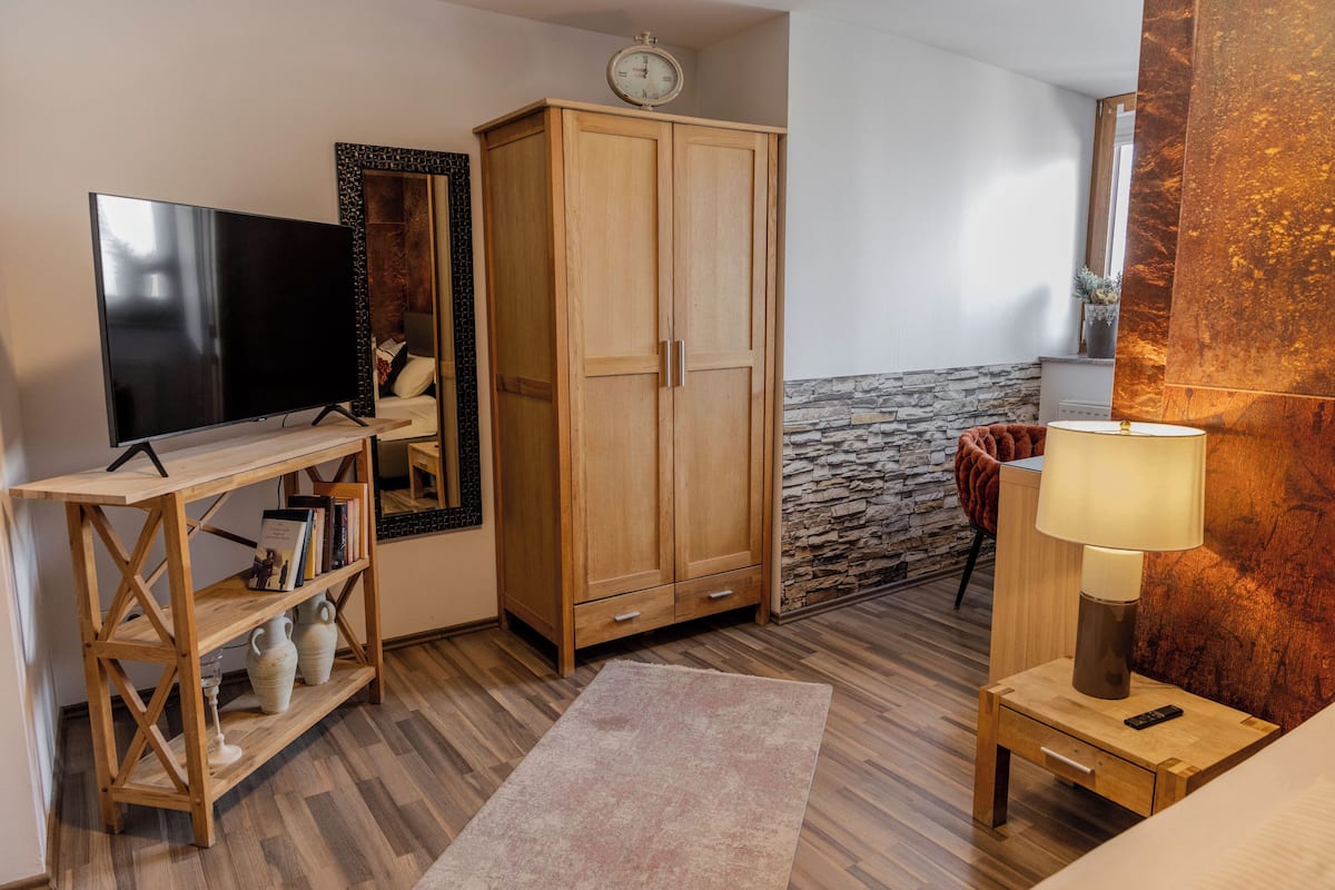 Une chambre avec une télévision, une armoire en bois, un mur en pierre et une table de chevet avec une lampe.