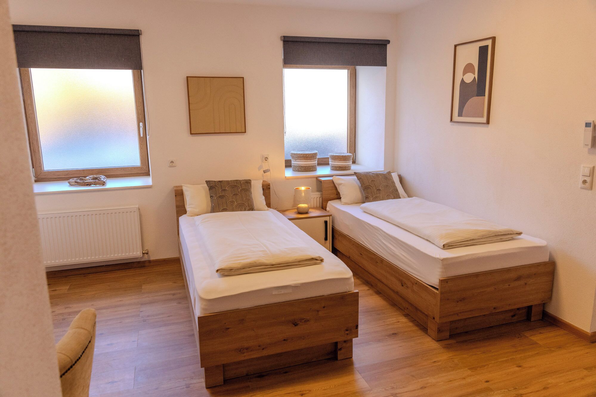 Un dormitorio con dos camas de madera, una ventana con vistas, un radiador y un cuadro enmarcado en la pared.