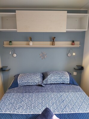 Une chambre à coucher comprenant un lit, deux lampes fixées au mur, une étagère avec des objets décoratifs et un luminaire circulaire fixé au mur.