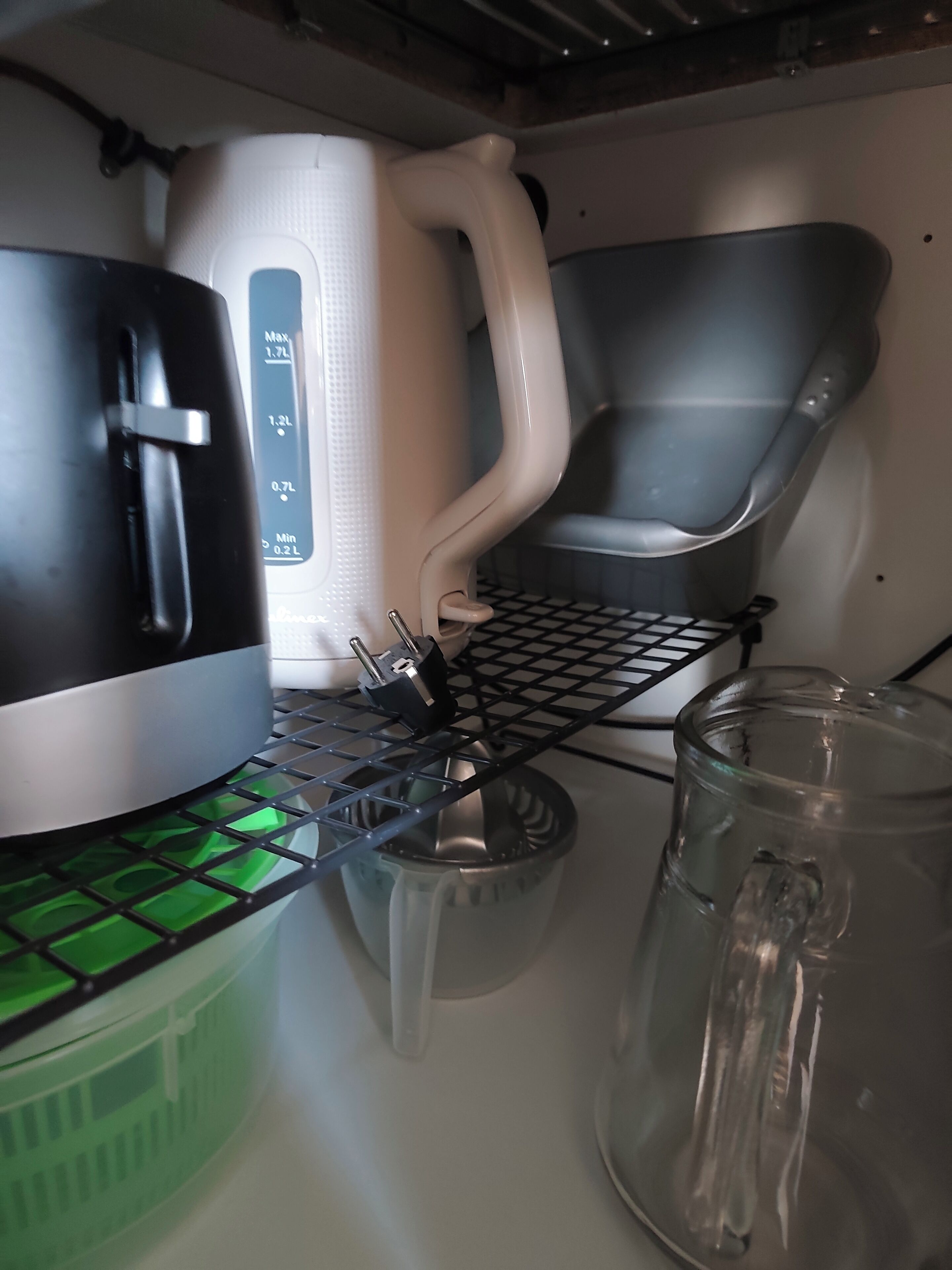 A kitchen area with a kettle, a coffee maker, a glass pitcher, and a metal rack.