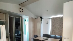 Un espace de vie compact comprenant une table à manger, un canapé, un coin cuisine et une porte donnant sur une autre pièce.