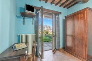 Una habitación con puerta de madera, un radiador, estante con televisor y vista al exterior.