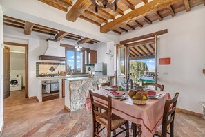 Una cocina con una isla de piedra, vigas de madera en el techo y un comedor con una mesa dispuesta para dos.