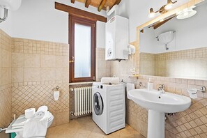 Une salle de bain équipée d’un lave-linge, d’un évier et d’une fenêtre.