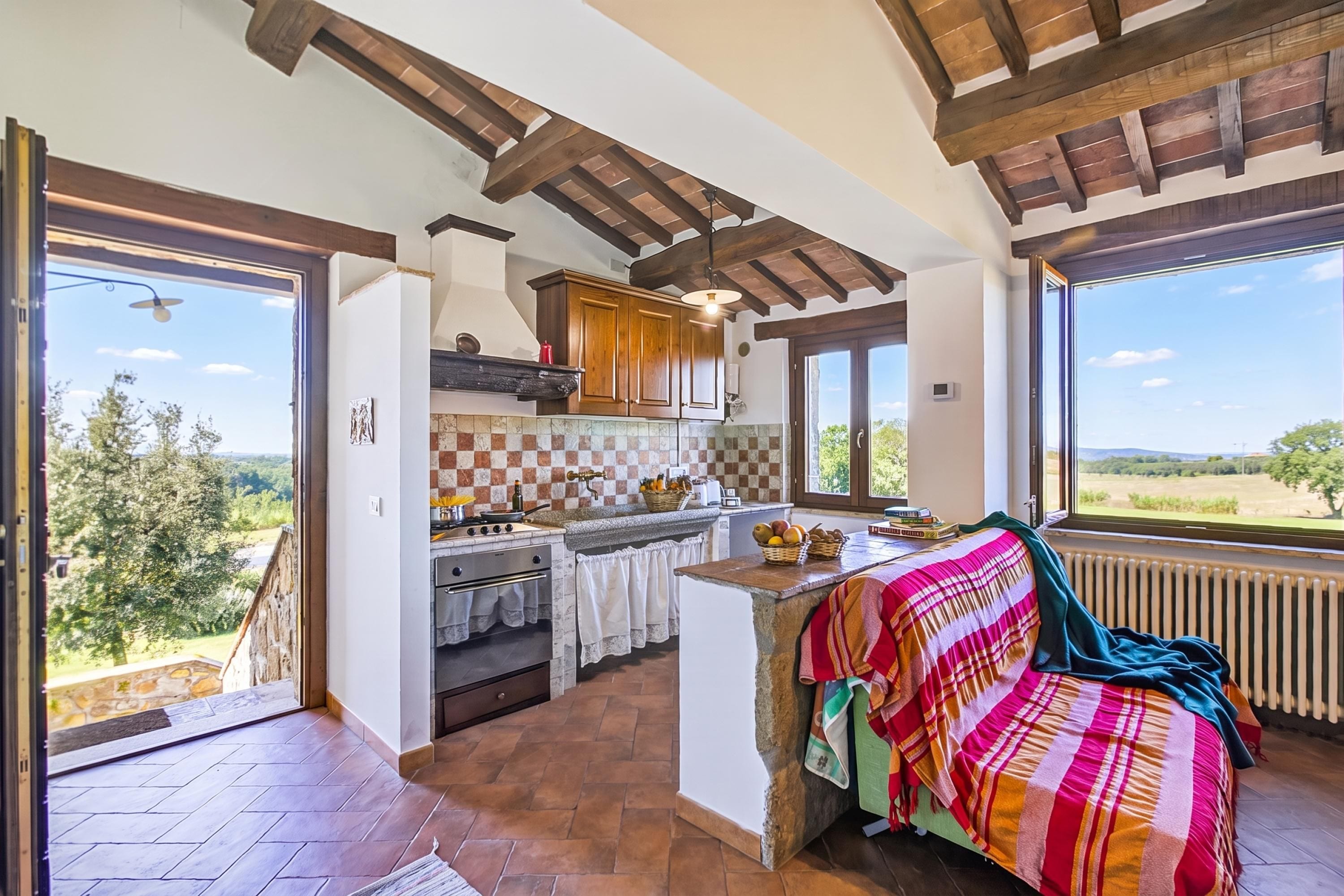 Un'ampia cucina con un piano di lavoro in pietra, mobili in legno e una grande finestra vista sulla campagna.