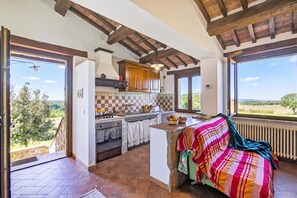 A spacious kitchen with a stone countertop, wooden cabinets, and a large window offering a view of the countryside. - Le Sorgenti House (Pitigliano)