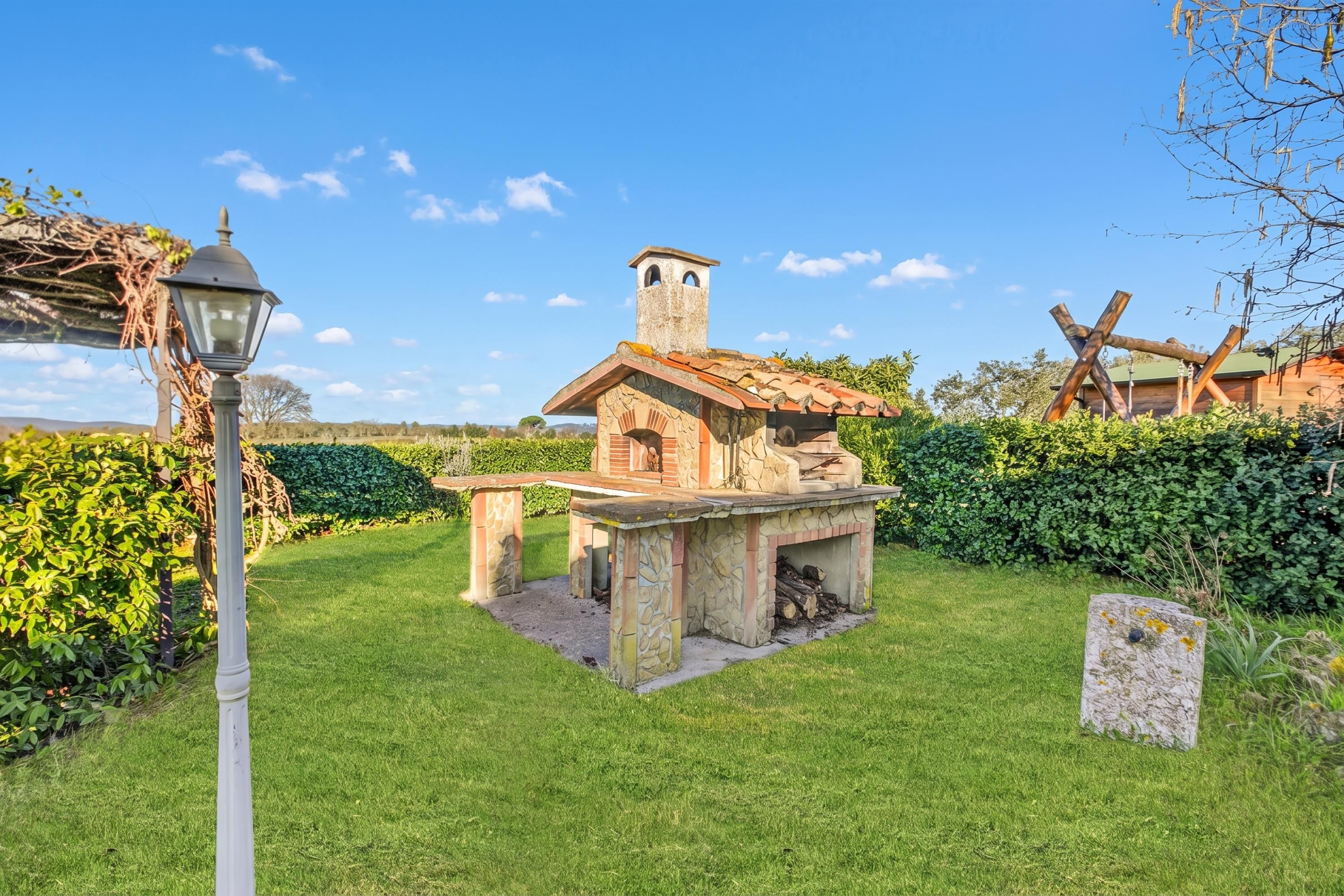 A stone-built outdoor kitchen with a chimney, surrounded by a well-maintained lawn and hedges.