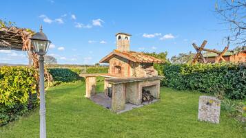 A stone-built outdoor kitchen with a chimney, surrounded by a well-maintained lawn and hedges.