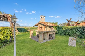 A stone-built outdoor kitchen with a chimney, surrounded by a well-maintained lawn and hedges.