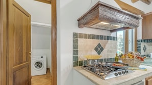 A kitchen with a stove, a washing machine, and a window with a view. - Le Sorgenti House (Pitigliano)