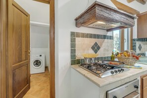 A kitchen with a stove, a washing machine, and a window with a view. - Le Sorgenti House (Pitigliano)