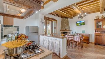 A kitchen with a gas stove, a dining area with a table and chairs, and a stone fireplace.