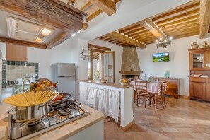Cozinha com fogão a gás, área de refeições com mesa e cadeiras, e lareira de pedra.