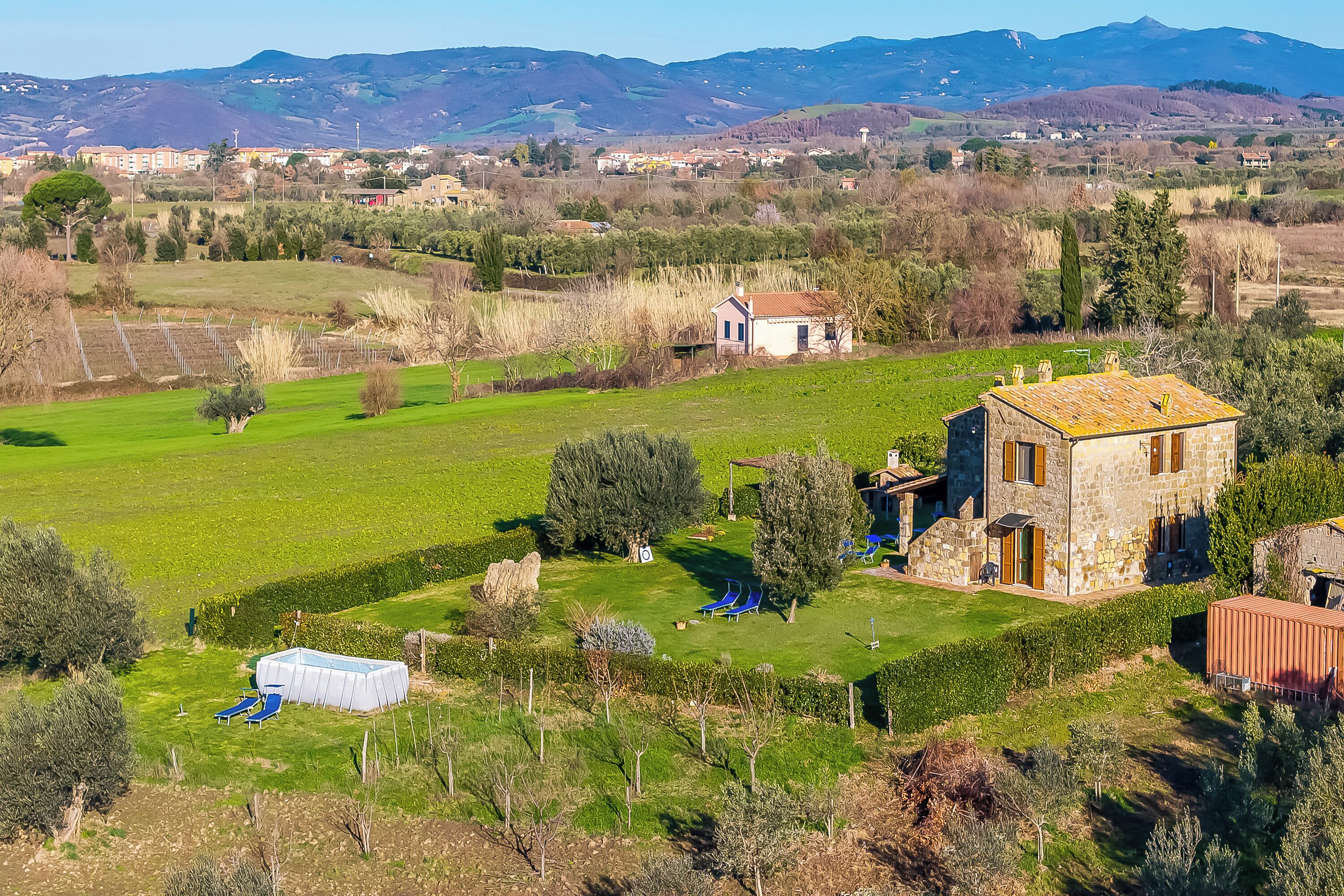 Un paysage rural avec une maison en pierre, une piscine et une vue dégagée sur les montagnes lointaines.