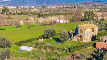 Paisaje rural con una casa de piedra, una piscina y una vista despejada de montañas distantes.