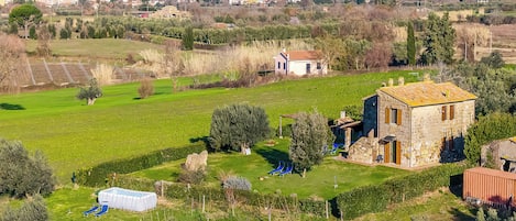 A rural landscape with a stone house, a swimming pool, and a clear view of distant mountains.