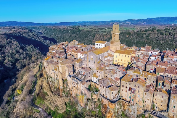 A historic town with stone buildings, a prominent tower, and a river. - Le Sorgenti House (Pitigliano)