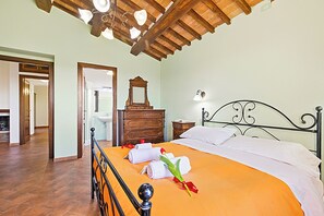Un dormitorio con techo de madera, una cama con colcha naranja, un aparador de madera y una mesita de noche con lámpara.