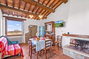 A cozy room with a dining table, chairs, a fireplace, and a television mounted on the wall. - Le Sorgenti House (Pitigliano)