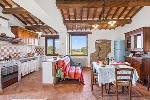 A rustic kitchen with a stone wall, wooden beams, and a view of the countryside. - Le Sorgenti House (Pitigliano)