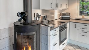 Eine moderne Küche mit Kaminofen, Edelstahlgeräten und weißen Schränken.