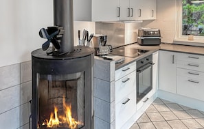 A modern kitchen with a wood-burning stove, stainless steel appliances, and white cabinetry. - 3 bedroom amazing home in Ringkøbing (Ringkøbing)