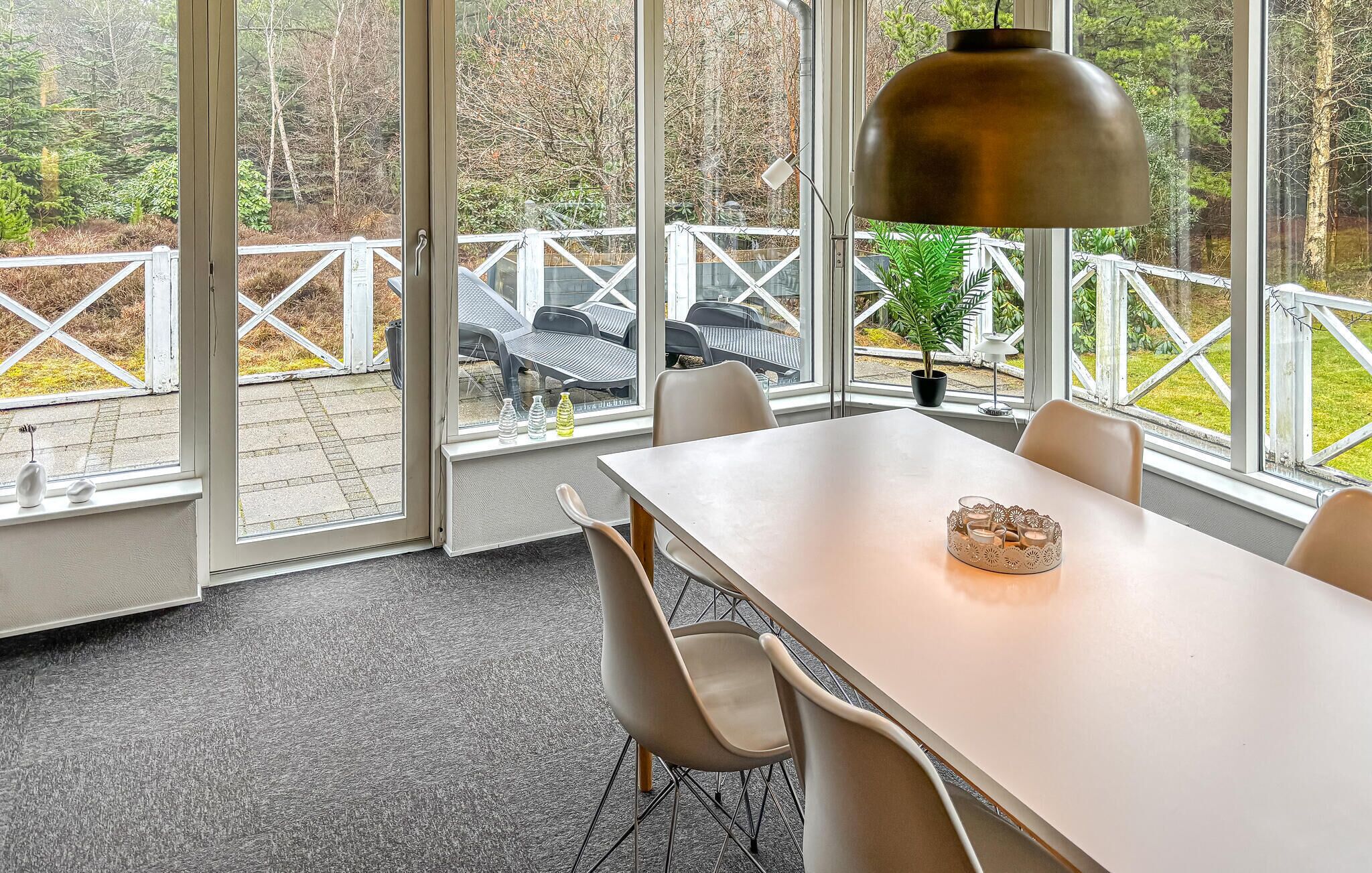 A dining area with a table, chairs, a pendant light, and a view of outdoor seating and trees.