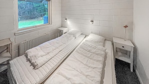 Ein Zimmer mit einem Einzelbett, einer weißen Ziegelwand, einem Fenster mit Blick auf einen Garten und einem Heizkörper unter dem Bett.