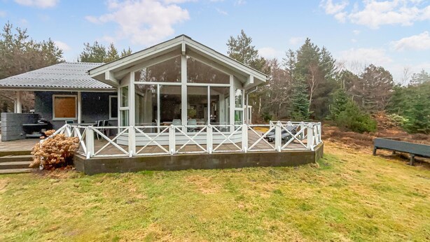 Eine Lodge mit überdachter Terrasse, ein kleines Gebäude mit Schornstein und ein grüner Rasen.