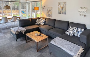 A modern living room with a sectional sofa, a coffee table, and a dining area with chairs. - 3 bedroom amazing home in Ringkøbing (Ringkøbing)