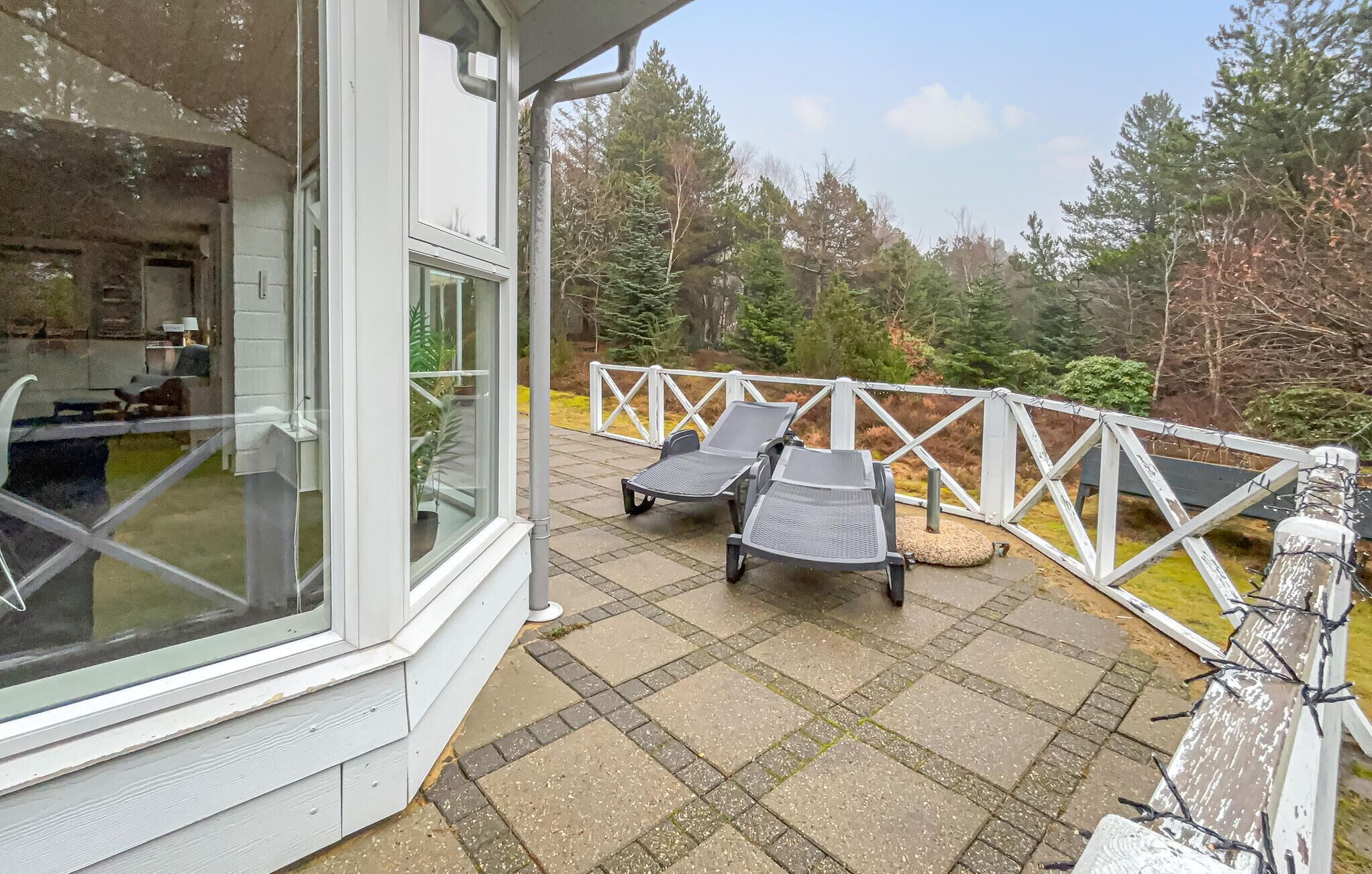 Eine Terrasse mit zwei Loungesesseln, einem weißen Geländer und Blick auf Bäume.